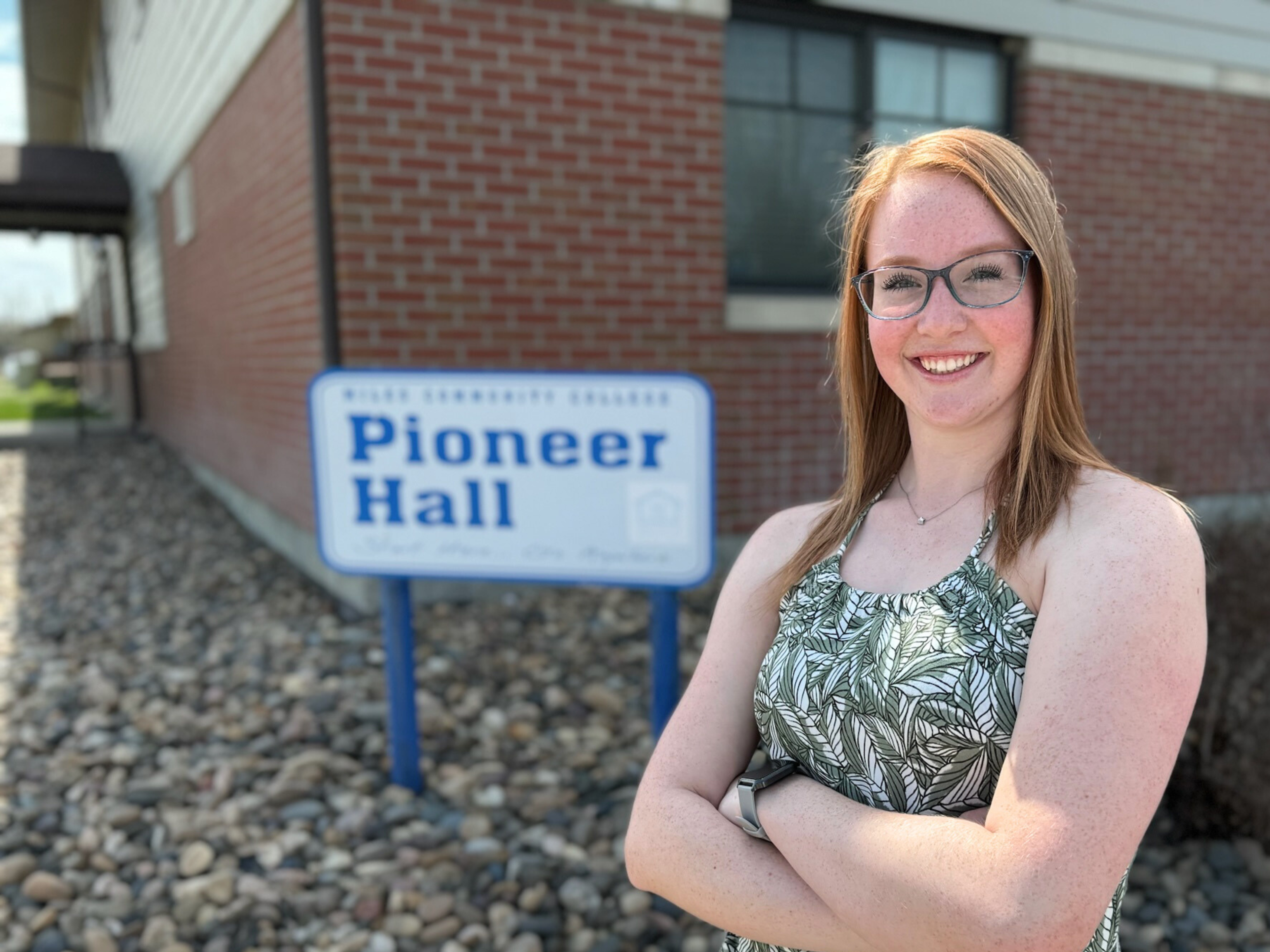 Adult smiling standing by sign that reads Pioneer Hall