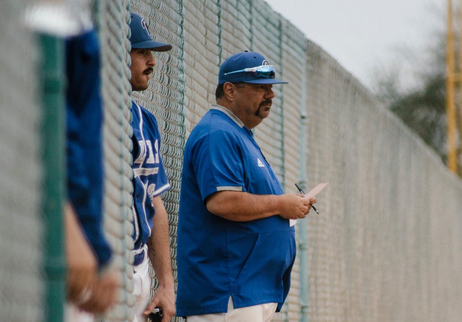 Image of male baseball coach, male baseball play in foreground